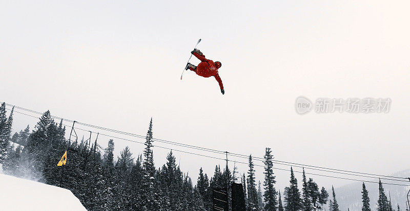 在科罗拉多州博尔德附近的埃尔多拉滑雪度假村，一个滑雪者在一个多雪的，阴天里，在森林和滑雪跳跃的背景下，尝试一个“背部Rodeo 540西瓜”的跳跃技巧